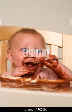 Il bambino nel seggiolone rendendo pasticcio con budino di cioccolato Foto Stock