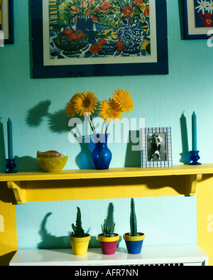 Close up di orange gerbera in vaso blu sul ripiano di colore giallo al di sopra di tre piccoli cactus in vasi colorati Foto Stock