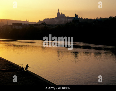 Una vista del torreggiante cattedrale di San Vito nel Castello di Praga su una collina sopra il fiume Moldava e un pescatore al tramonto Foto Stock