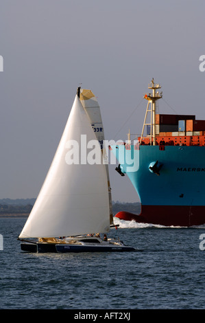 Uno yacht a vela sotto la prua di una grande nave portacontainer nel canale di thorn rotte di navigazione nel solent Foto Stock