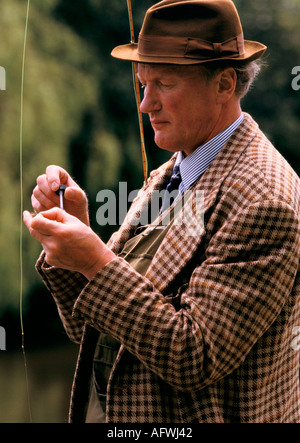 Giacca in tweed UK cappello marrone fedora elegante uomo pesca alla trota che mette una mosca sulla sua linea. John nasce uno sportivo professionista dell'Hampshire degli anni '1980 in Inghilterra Foto Stock