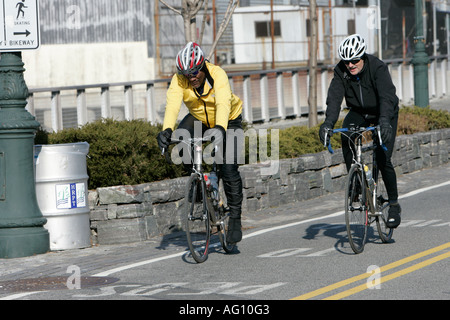 Il nero di mezza età nel maschio giallo in alto e maschio bianco nella parte superiore nera sulla bici da corsa che esercitano su bikeway Foto Stock