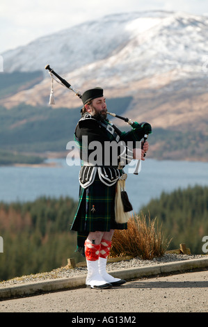 Scottish piper riproduzione di cornamusa sopra Loch Tulla, Highlands scozzesi con montagne innevate sullo sfondo Foto Stock