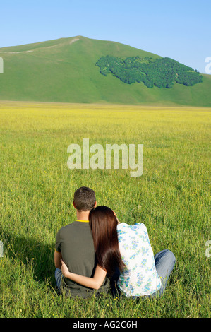 Coppia giovane seduto in campo di montagna, vista posteriore Foto Stock