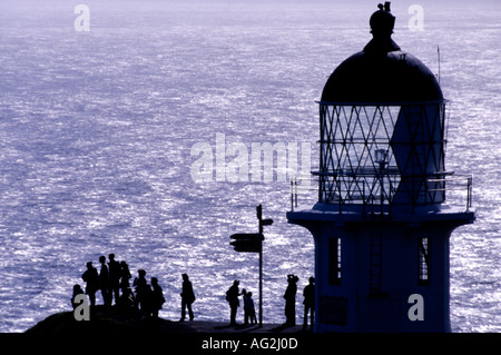 Cape Reinga Lighthouse stagliano contro il mare di Tasmania con figure e segnaletica al di sotto di Isola del nord della Nuova Zelanda Foto Stock