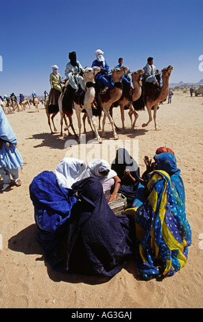 Algeria Tamanrasset persone della tribù Tuareg uomini a cavallo cammello mentre le donne sedute sulla sabbia durante il festival denominato Tafsit Foto Stock