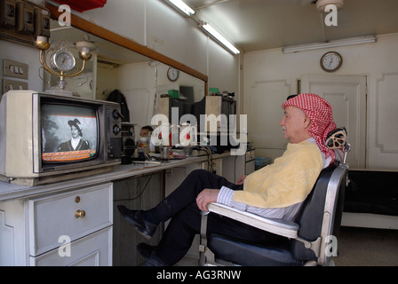 Un barbiere wairing un tradizionale rosso e bianco a scacchi keffiyeh seduti in un salone di parrucchiere in Amman Giordania Foto Stock