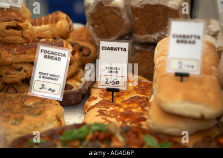 Vari tipi di pane di specialità tra cui la ciabatta e focaccia compresi ingredienti su un pane e una fetta di torta in stallo Foto Stock