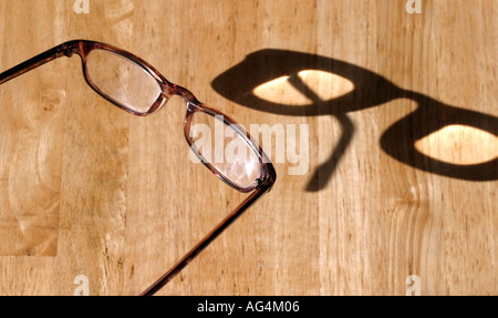 Un paio di occhiali da lettura fortemente illuminate dalla luce del sole e il casting di un abstract ombra Foto Stock