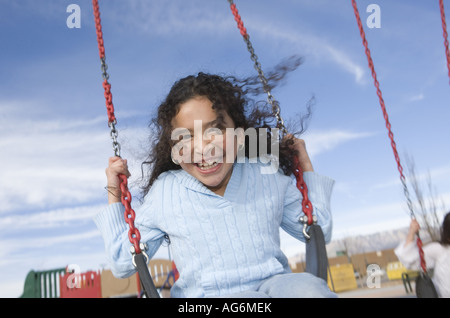 9 anno vecchia ragazza swinging all aperto con vento che soffia i suoi capelli contro il cielo blu Foto Stock