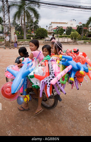 Laos famiglia su un motociclo in Vientiane con loro dei giocattoli gonfiabili per la vendita Foto Stock