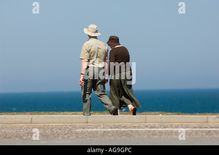 Coppia di anziani holding hands passeggiate in riva al mare in una giornata di sole Foto Stock