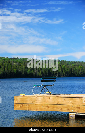 Banco vuoto sul dock di legno rivolta verso l'acqua blu Foto Stock