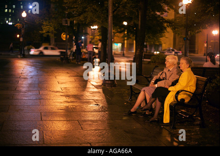 Due donne anziane siedono su una panchina nel parco di notte in plaza a Faneuil Hall Boston MA Foto Stock
