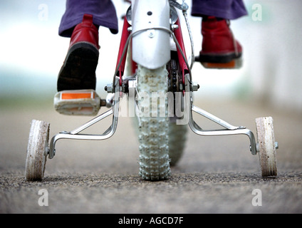 Un giovane bambino su una bicicletta con stabilizzanti o stabilizzanti o ruote di formazione Foto Stock