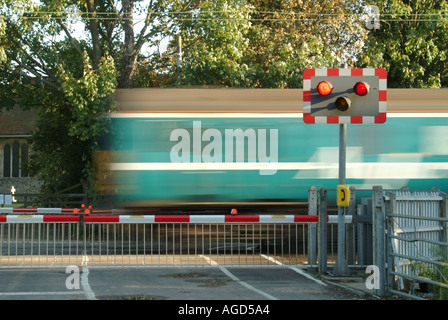 I binari ferroviari rosso lampeggiante spia livello di segno attraversando i cancelli di barriera stradale del paese treni passeggeri motion blur Margaretting Essex England Regno Unito Foto Stock