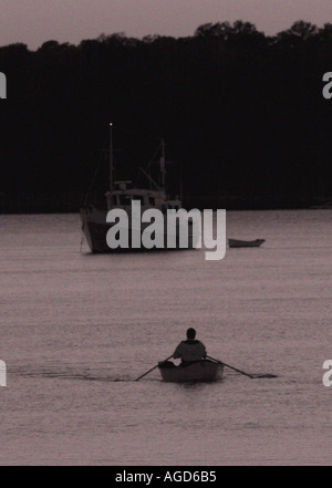 Uomo su una barca a remi al crepuscolo sulle acque calme di Beaufort, South Carolina, Stati Uniti. Una tranquilla atmosfera di bassa campagna con una luce soffusa che si riflette sull'acqua. Foto Stock