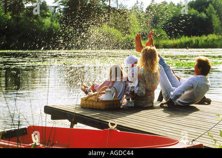 Famiglia di quattro persone con Cesto picnic calci acqua sul molo sul lago in Svezia Foto Stock