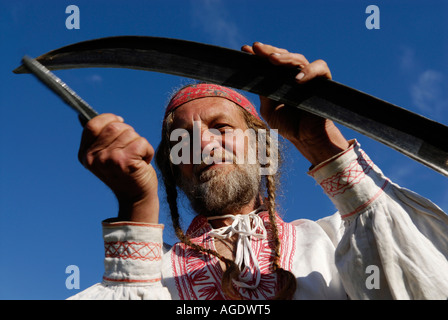 Immagine di stock di un uomo con una pietra abrasiva per affilare una falce la lama durante il taglio di un campo di fieno in New Brunswick Canada Foto Stock