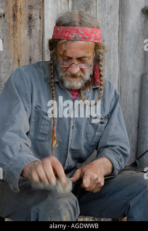 Stock a immagine di un uomo con lunghi capelli intrecciati la pallinatura e affilatura o la levigatura di una lama di falce Foto Stock