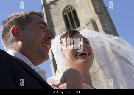 Bassa angolazione di sorridenti sposi camminare sul telaio - con vista sullo sfondo della lingua inglese chiesa parrocchiale torre Foto Stock