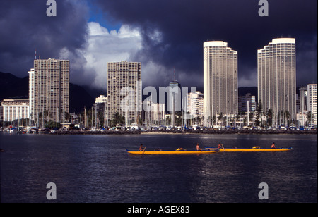 Alta scuola di canoa outrigger squadre pratica all'entrata di Ala Wai Canal con una tempesta costruzione sulle colline Foto Stock