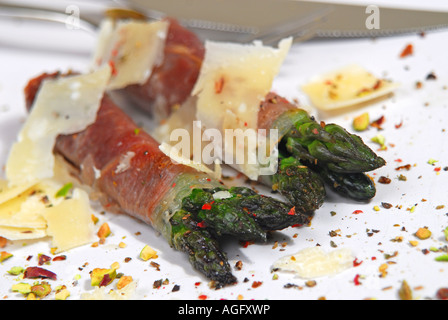 Gli asparagi avvolti nel prosciutto di Parma con scaglie di parmigiano, frantumato di pistacchi e la terra rossa, verde e pepe nero. Foto Stock