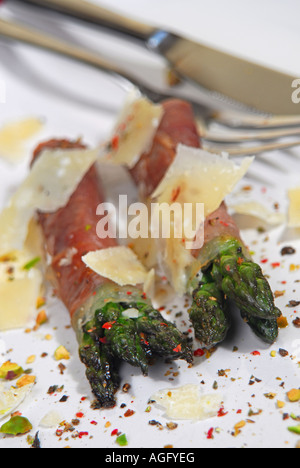 Gli asparagi avvolti nel prosciutto di Parma con scaglie di parmigiano, frantumato di pistacchi e la terra rossa, verde e pepe nero. Foto Stock