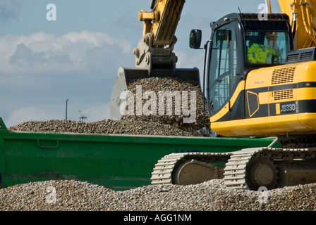 Escavatore giallo spostando le scandole in autocarro verde lavorando sulla spiaggia "moto-pala' Foto Stock