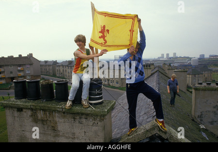 I bambini piccoli tengono una bandiera scozzese, la bandiera del leone rampante della Scozia sopra le loro teste dai tetti di un blocco enorme del consiglio degli appartamenti Glasgow 1980 Foto Stock