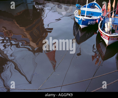 La riflessione di poppa di Endeavour replica e due barche da pesca, Whitby, North Yorkshire, Inghilterra, Regno Unito Foto Stock