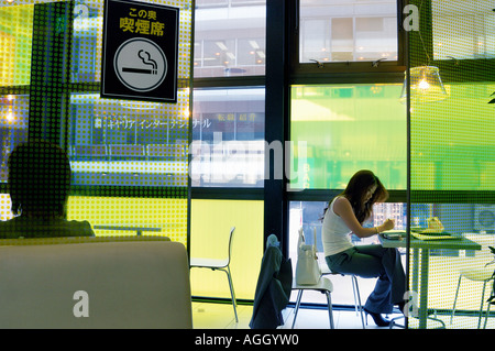 Ragazza giovane studia in camera per fumatori in un fast food place, Tokyo, Giappone Foto Stock