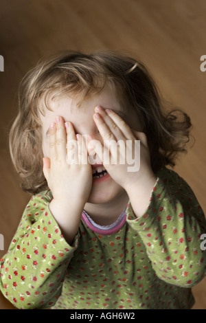 Un giovane bambino nascondersi dietro le mani Foto Stock