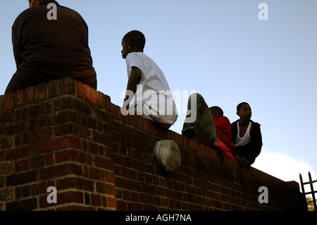 Giovani ragazzi al di fuori della scuola e la noia alimentato fino seduti sulla parete in Brixton a sud di Londra in attesa. Foto Stock