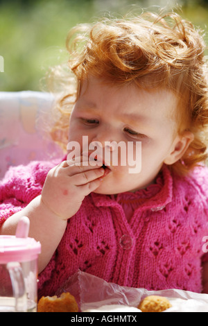 Una alimentazione dei bimbi se stessa in una sedia alta utilizzando un vassoio Foto Stock