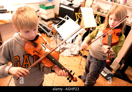 Un fratello e una sorella che fare il loro quotidiano la pratica del violino in un affollato tipica classe media famiglia inglese e soggiorno Foto Stock
