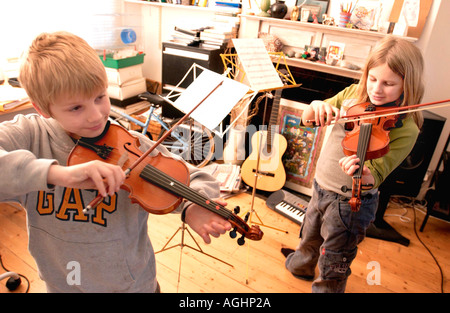 Un fratello e una sorella che fare il loro quotidiano la pratica del violino in un affollato tipica classe media famiglia inglese e soggiorno Foto Stock