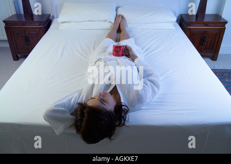 Premurosa ragazza sul letto trattiene mug Foto Stock