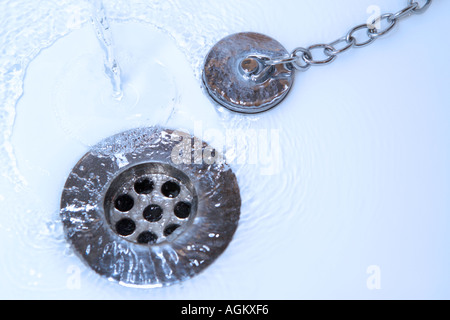 L'acqua che scorre verso il basso il foro del tappo di close-up di illuminazione blu Foto Stock