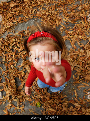 Bambina guardando la telecamera carino bambina indossa jeans e maglietta rossa vista dalla cima Foglie di autunno sul terreno Autumna Foto Stock