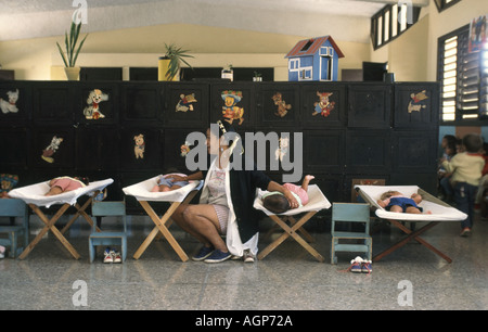 Donna cubana tendente a bambini molto giovani prendendo la loro mattinata pan a asilo nido o alla scuola materna nel centro di Havana Cuba Foto Stock