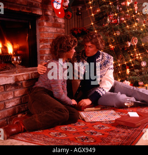 Natale in scena con la giovane coppia romantica a giocare a scrabble davanti a un caminetto con decorate albero in background Foto Stock