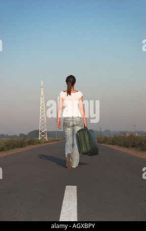 Giovane donna a piedi lungo la strada che porta la valigia, vista posteriore Foto Stock