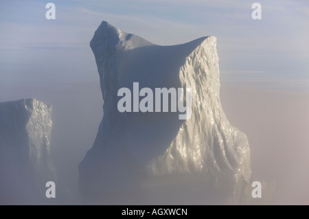 Enormi iceberg drammatico luccicanti nel tardo pomeriggio di sole con bassa nebbia mare galleggianti intorno loro fuori costa sud-ovest della Groenlandia Foto Stock