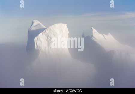 Enormi iceberg drammatico luccicanti nel tardo pomeriggio di sole con bassa nebbia mare galleggianti intorno loro fuori costa sud-ovest della Groenlandia Foto Stock