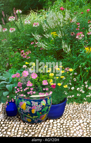 Di acciottolato bianco terrazza con grandi Oriental vasi di ceramica con colori corrispondenti al giardino di fiori selvaggi di rosa bianco e giallo Foto Stock