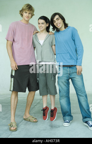 Tre giovani amici, teen girl permanente sulla tiptoes tra due amici maschi a piena lunghezza ritratto Foto Stock