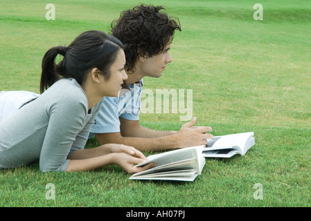 Coppia giovane sdraiato sul prato con libri, guardando fuori del telaio Foto Stock