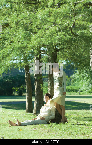 Giovane sotto agli alberi, uomo seduto sull'erba mentre la donna sta Foto Stock