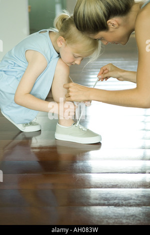 Madre aiutare bambina tie lacci delle scarpe Foto Stock